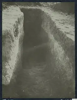 Excavation of Tomb 25 at Marion: a deep stepped cutting in earth with grass and stones at the top edges.