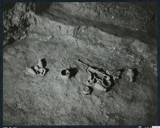 Tomb 25 at Marion during excavation, with small pottery vessels and fragments lying on the rock floor.