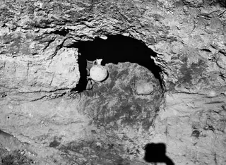 Opened niche in a rock-cut tomb wall with a small handled jug lying inside it