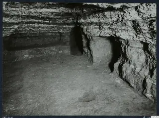 Interior of Tomb 25 at Marion, with layered rock walls, a recess in the right-hand wall and an earth floor