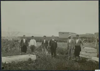 Six men stand in a grassy field beside a rectangular stone trough and stacked stone slabs at Marion
