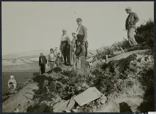 People standing among scrub on a hillside at Marion, with an earth heap and wooden stakes in the foreground