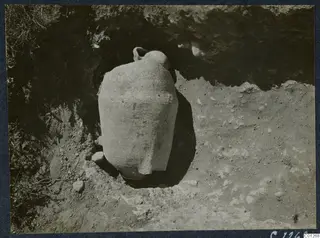 Large pale pottery vessel standing in an excavated cut at Marion, with stones around it