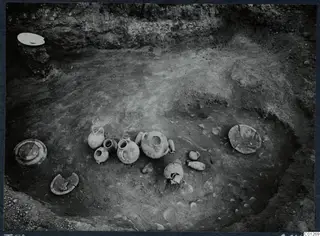 Tomb 50 at Marion during excavation, with pottery vessels and plates lying on the floor among scattered stones