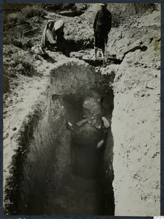 Tomb 56 at Marion during excavation, with two seated people and a standing man at the edge of the cut
