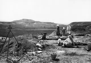 Women and a dog working at the Marion excavation, with a tripod instrument and metal buckets in the foreground