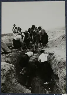 Workers digging in a deep cut at Tomb 53 at Marion, with a group standing along the edge.