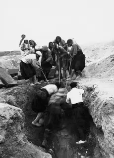 Workers digging in the trench at Tomb 53 at Marion, with a group standing on the bank behind them.