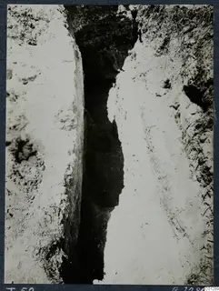 Narrow excavated cutting at Marion, with pale earth walls and a dark deep slot in the middle, during excavation of Tomb 52.