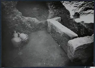 Tomb 41 at Marion: interior of a tomb chamber with cut stone blocks and two vessels against the wall