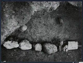 Tomb 41 at Marion: a row of stones and small vessels on an excavated floor