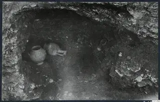 Interior of Tomb 59 at Marion during excavation, with two pottery vessels and loose stones on the floor of the cut.