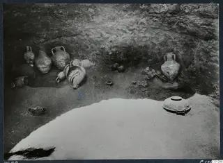 Handled pottery vessels and bowls lying on the floor of Tomb 58 at Marion during excavation.