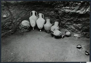 Tomb 57 at Marion during excavation, with a group of jars and bowls lying in place against a rock-cut wall