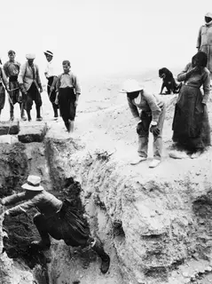 Workers at an excavation cutting, one man leaping down into the trench while others watch from the edge