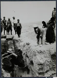 Workers and onlookers at the excavation of Tomb 53 at Marion, one man climbing down into a steep cut in the ground.