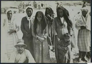 Group of women in headscarves and long dresses with a seated man and a small boy, at the excavation at Marion.