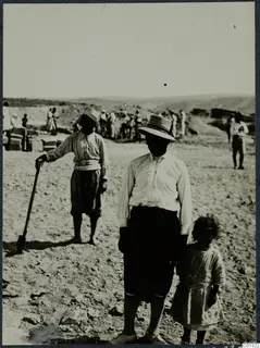 Two workers and a young girl on a dry excavation site at Marion, with more workers and stone blocks behind them.