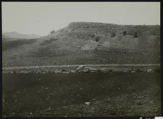 Eroded slope at Marion with dark openings cut into its face, a small group of people on the slope, and stones in the foreground.