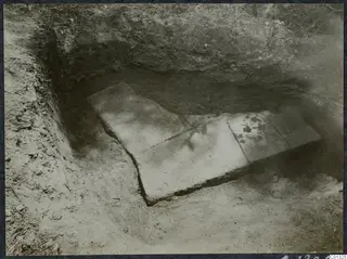 Excavation trench at Marion with large flat stone slabs lying in the pit and grass along the top edge.