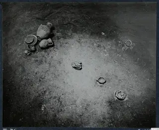Excavated tomb floor at Marion with clay vessels, a shallow bowl and small rings lying in the soil