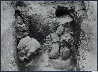 Excavation cutting at Marion with stones lying in a narrow trench between rough earth walls, with dark openings at the back