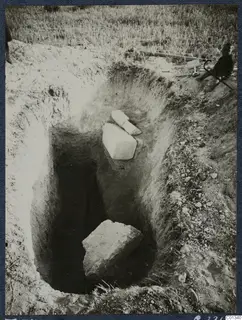 Tomb 74 at Marion during excavation: a deep rectangular cutting with stone blocks, and a seated person with tools at the edge