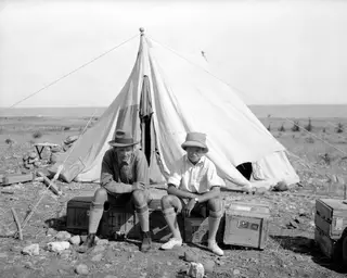 Two men sit on wooden crates in front of a large canvas tent at Marion.