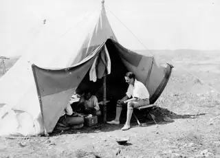 Men sitting at a large canvas tent on dry, stony ground at Marion, one man on a folding stool at right.