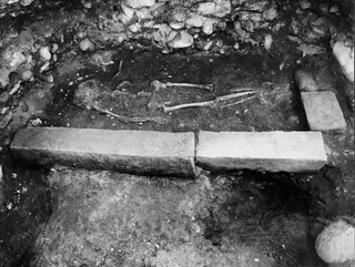 Skeleton lying in situ in Tomb 67 at Marion, with long stone slabs beside it.