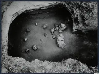 Tomb 63 at Marion during excavation, with small clay vessels set on the floor of a rock-cut chamber