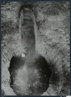 Tomb 70 at Marion during excavation: a stepped passage cut down into pale soil, opening to a dark tomb chamber.