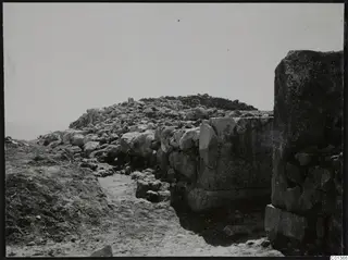 Nitovikla: loose stone rubble and a wall of large blocks at an excavation, with a tall upright stone at the right edge.