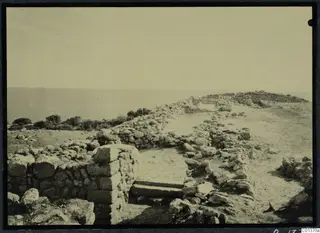 Stone walls, rubble and a short flight of steps on a bare hilltop at Nitovikla, with the sea beyond.