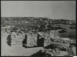 Stone walls and fallen blocks among scrub at Nitovikla, with hills behind.