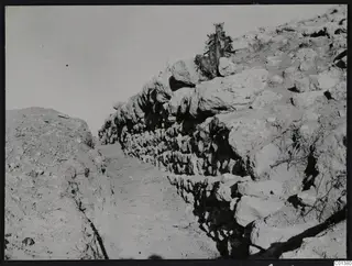 North enclosure wall at Nitovikla seen from the west, rough stone courses beside a dirt path