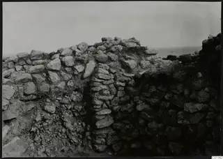 Stone wall foundations at Nitovikla, with sea visible on the horizon behind.