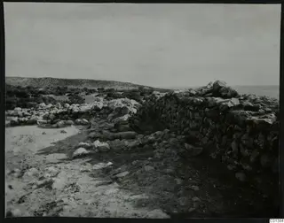 Stone wall and scattered rubble at Nitovikla, with low scrubby hills and the sea beyond