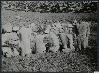 Weathered stone statues standing against a field wall at Oura