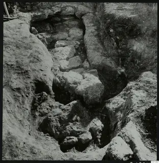 Excavation at Nitovikla on the Karpas Peninsula, with large stones in a trench and a pick in the top left corner.