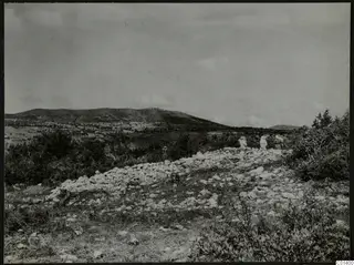Nitovikla on the Karpas Peninsula: scattered pale stones and scrub in the foreground, low hills behind, with people standing at right.