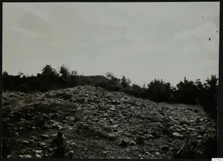 Rocky mound at Nitovikla on the Karpas, covered with loose stones and scrubby bushes under a cloudy sky.