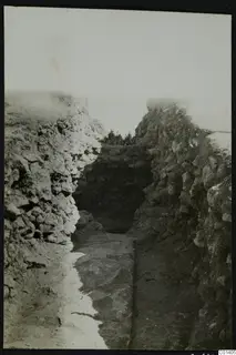Excavated trench between rough stone walls, with a flat stone slab on the floor and a dark recess at the far end