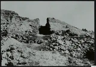 Excavated rocky hillside at Nitovikla with a dark opening in a cut rock face and scattered stones