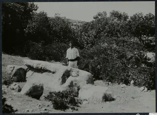 Man standing behind large pale stone blocks among scrub and trees on the Karpas peninsula.