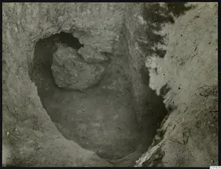 Excavation pit with a large stone lying in its upper part and tree roots at the edge, Kountoura Trachonia.