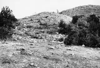Stone mound of Tomb 7 at Palaeoskoutella seen from the south-west, with a figure standing on its crest.