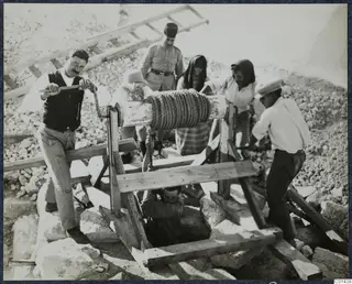 Men work a wooden windlass over a well at Vouni, lowering a man into the shaft