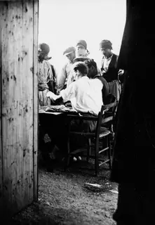 Seated man at a table at Vouni with a group of men in headcloths and caps standing around him