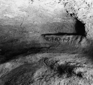 Interior of Tomb 14 at Ayios Iakovos, showing rock-cut walls, a ledge along the wall and an uneven floor.